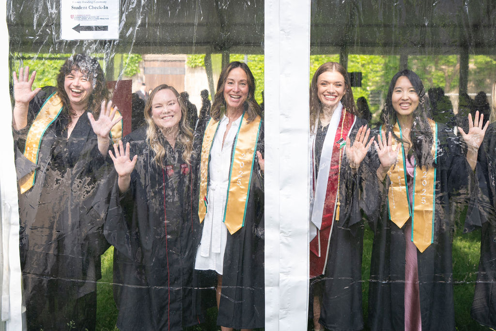 Five graduates inside the tent looking out smiling all in regalia