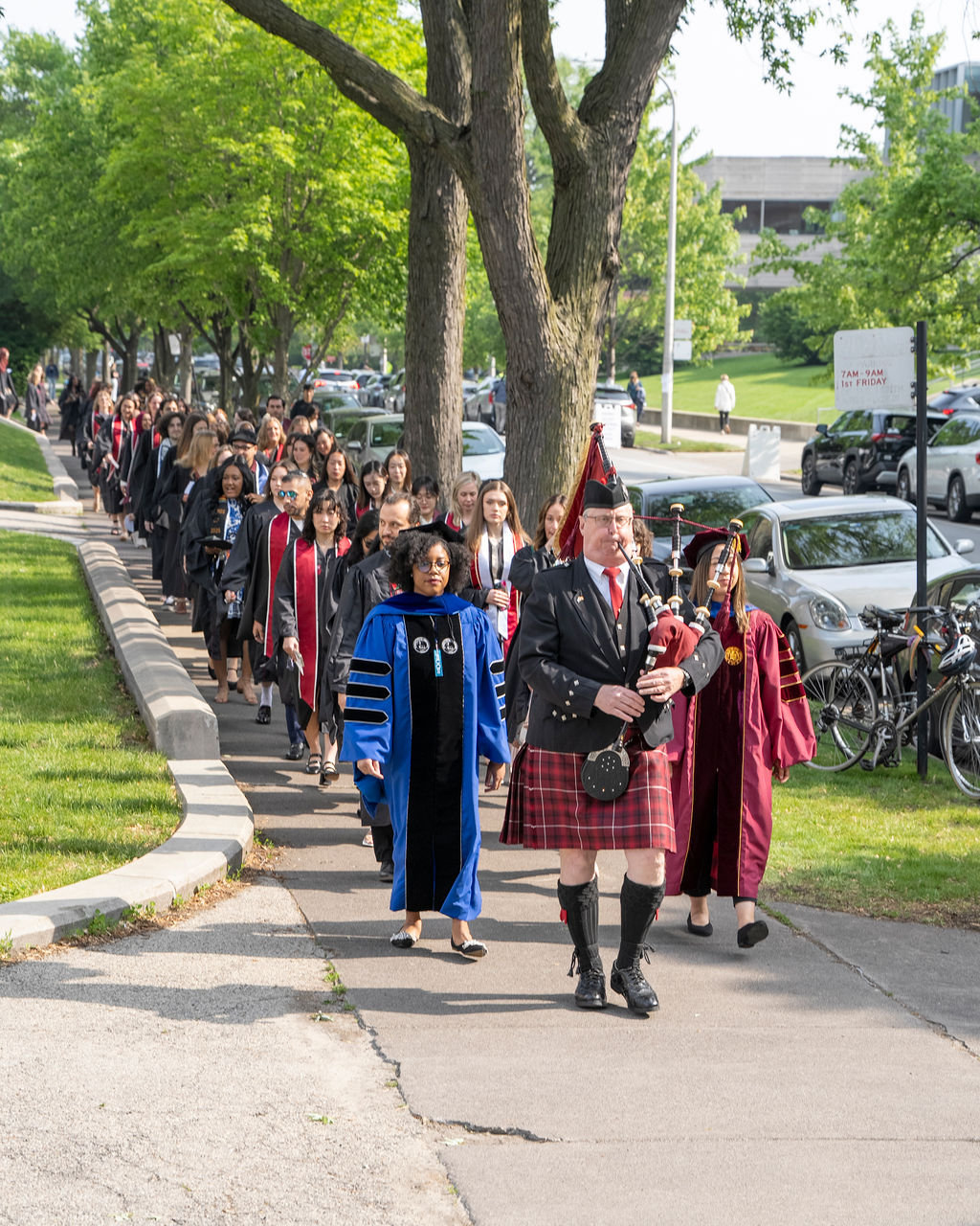 bag piper leading a group of graduates down the street in regalia