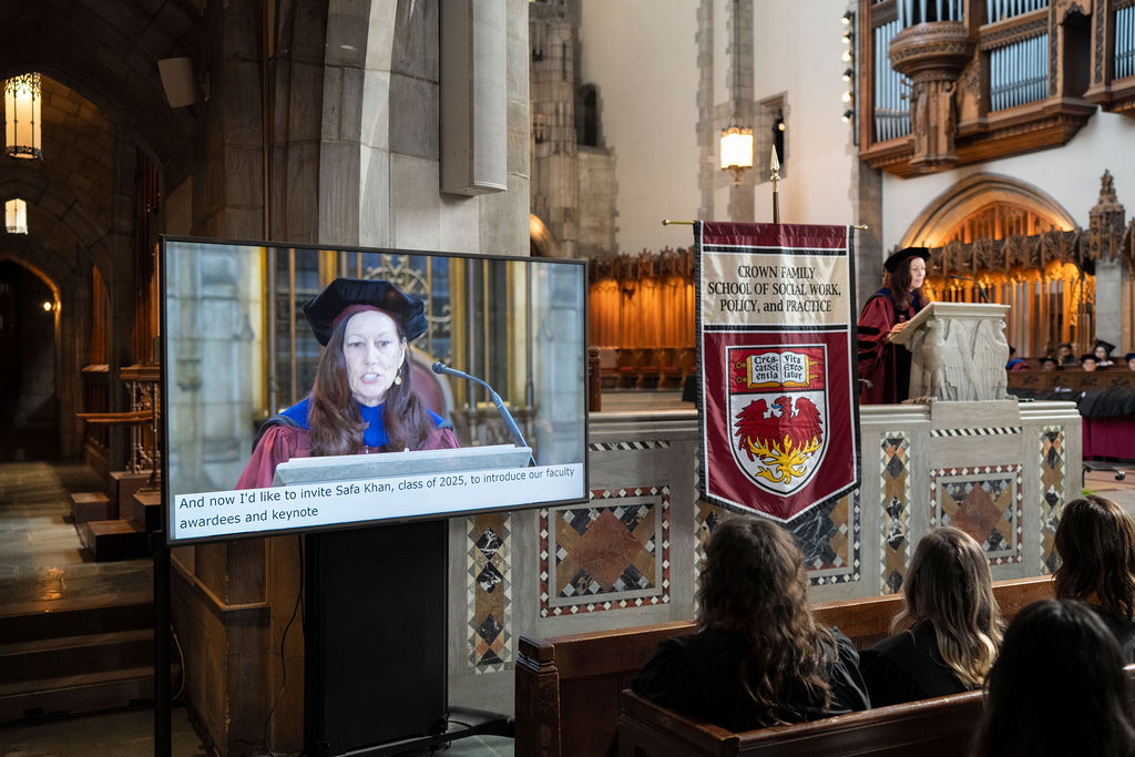 image of woman in graduation regalia speaking at podium with image also on monitor with close caption