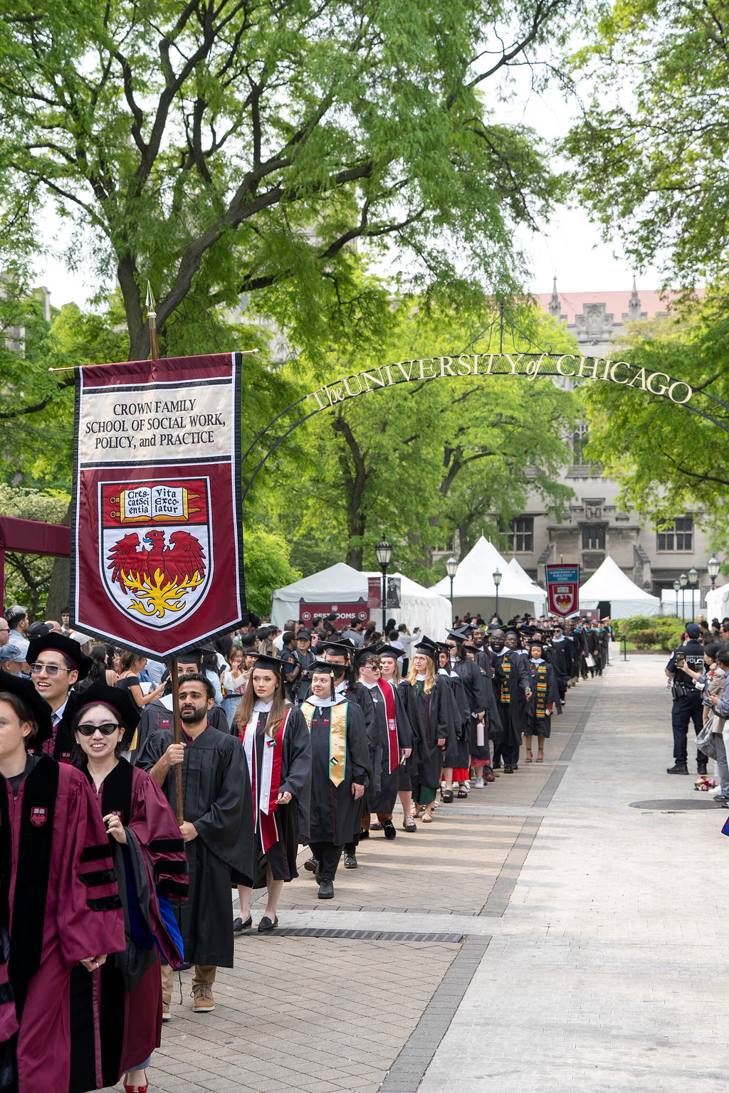 group of graduates line up outdoors with the Crown Family School flag