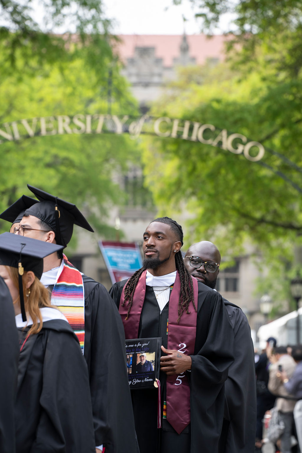 two male graduates in a line one with a maroon stole holding a picture album and the other with glasses directly behind him