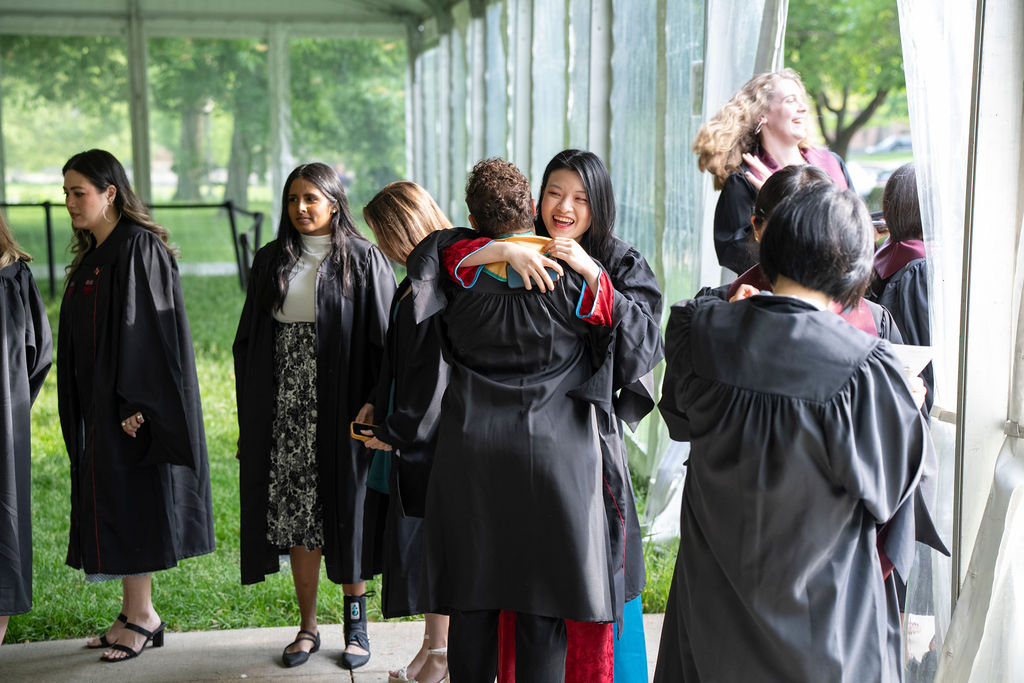 image of graduates hugging and smiling in regalia before the ceremony begins
