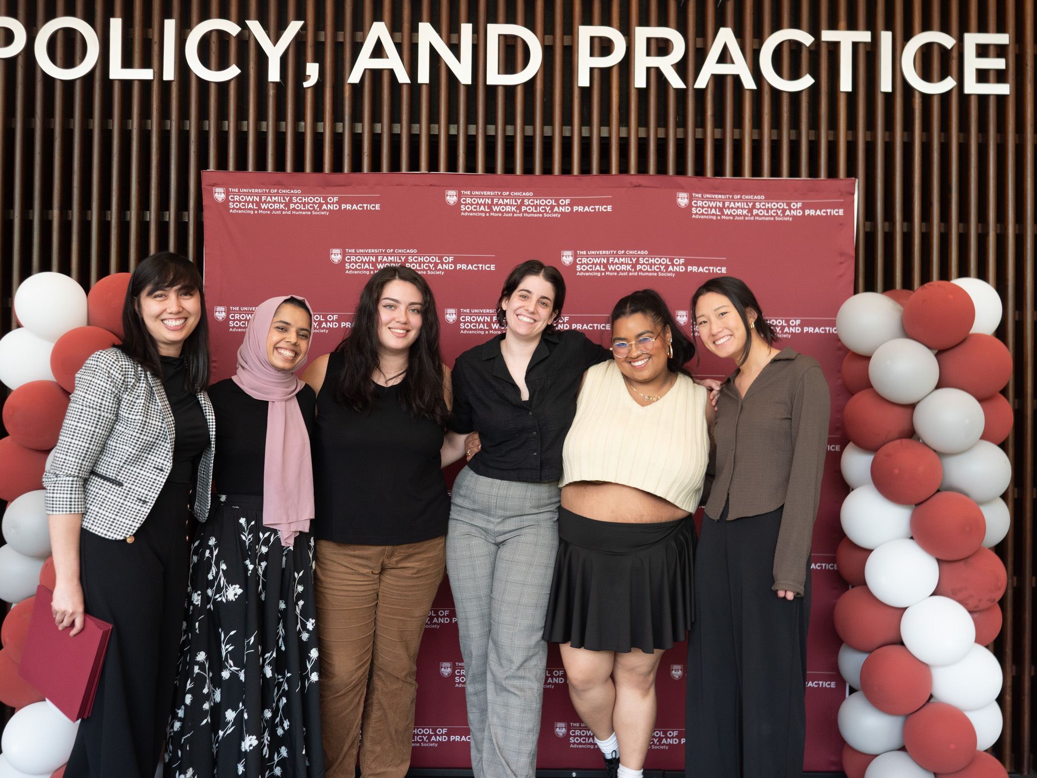 Image of group of six people standing in front of a maroon backdrop with balloons on both sides