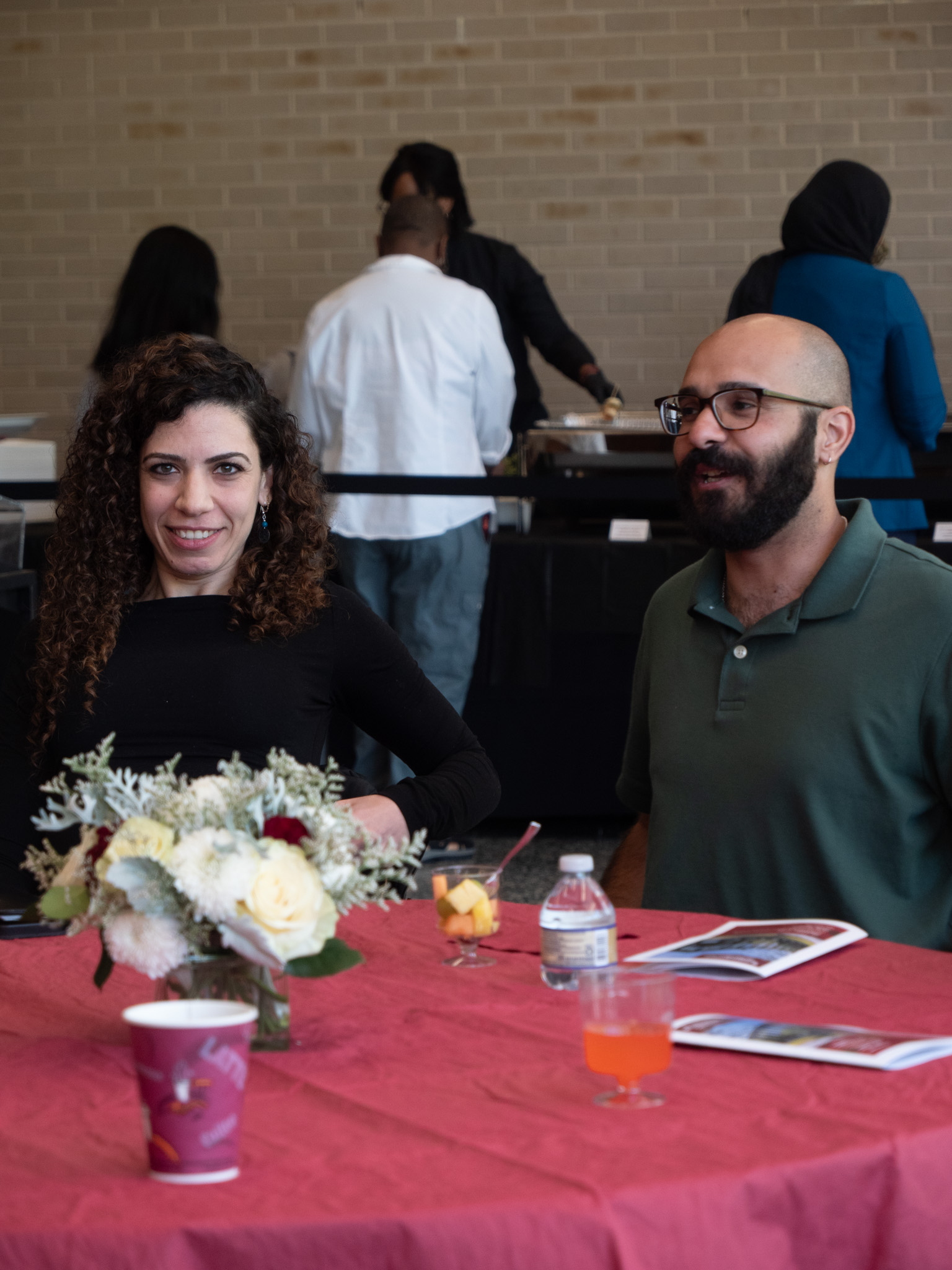 Image of people sitting at tables one in a black dress and another with grey suit 
