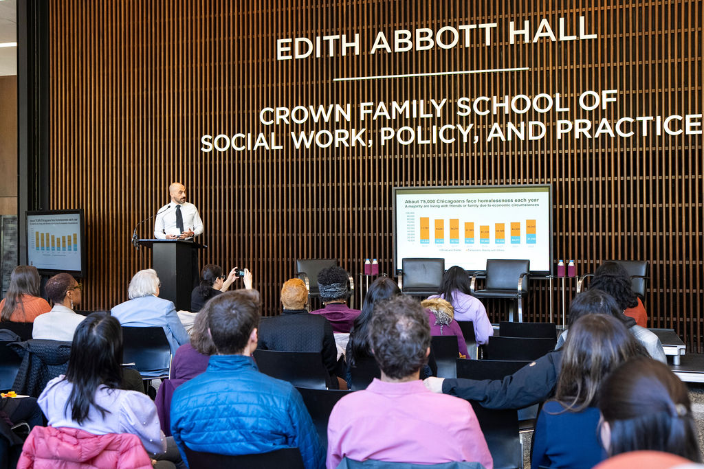 male standing at podium speaking with data slides at the Crown Family School