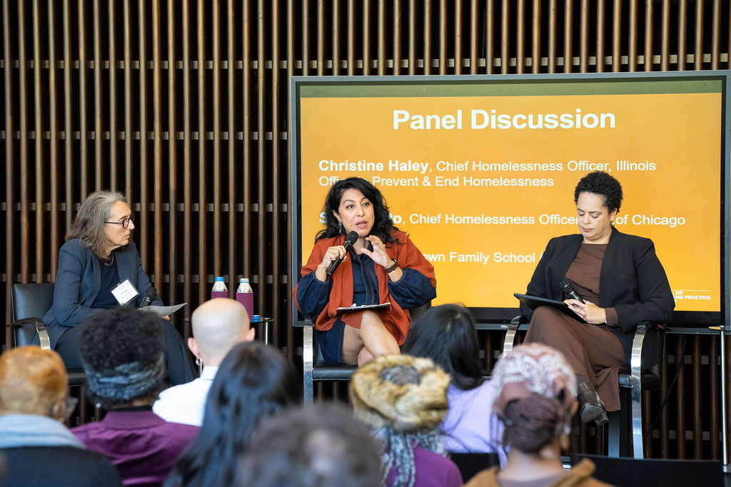 a group of 3 people sitting on a panel with one holding a mic speaking