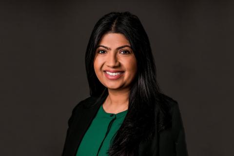 Hina Mahmood in a green blouse and black suit jacket against a gray background