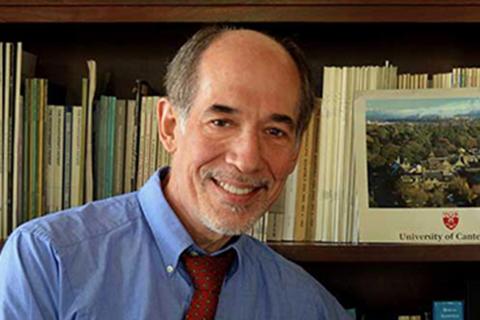 Jerry Brandell in a blue dress shirt and red tie in front of a bookcase