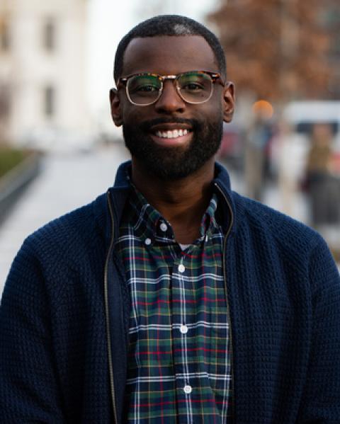 man in blue sweater with checkered shirt and glasses smiling