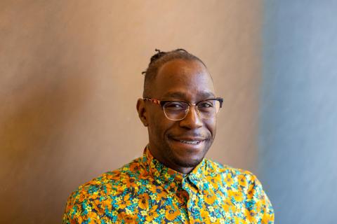 Man smiling in a yellow flower print shirt with glasses