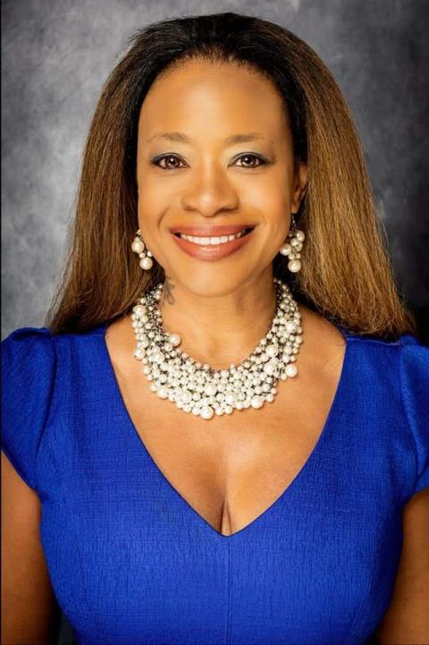 Photo shows headshot of woman with long light brown hair wearing a formal blue dress and sliver chunky necklace. 