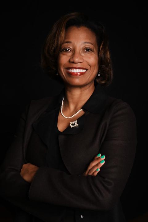 Photo shows woman standing in wearing a black suit and necklace