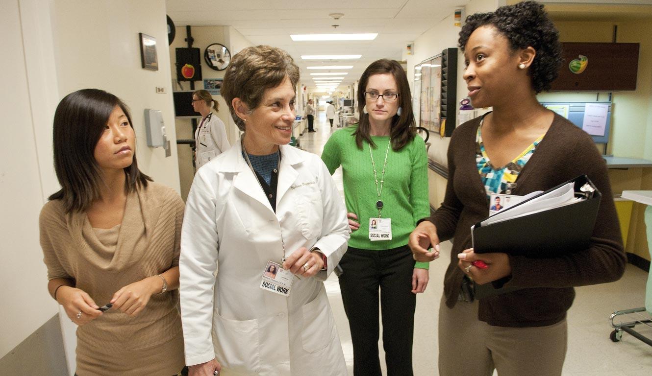 A person in a white lab coat with 3 other people in a hospital corridor