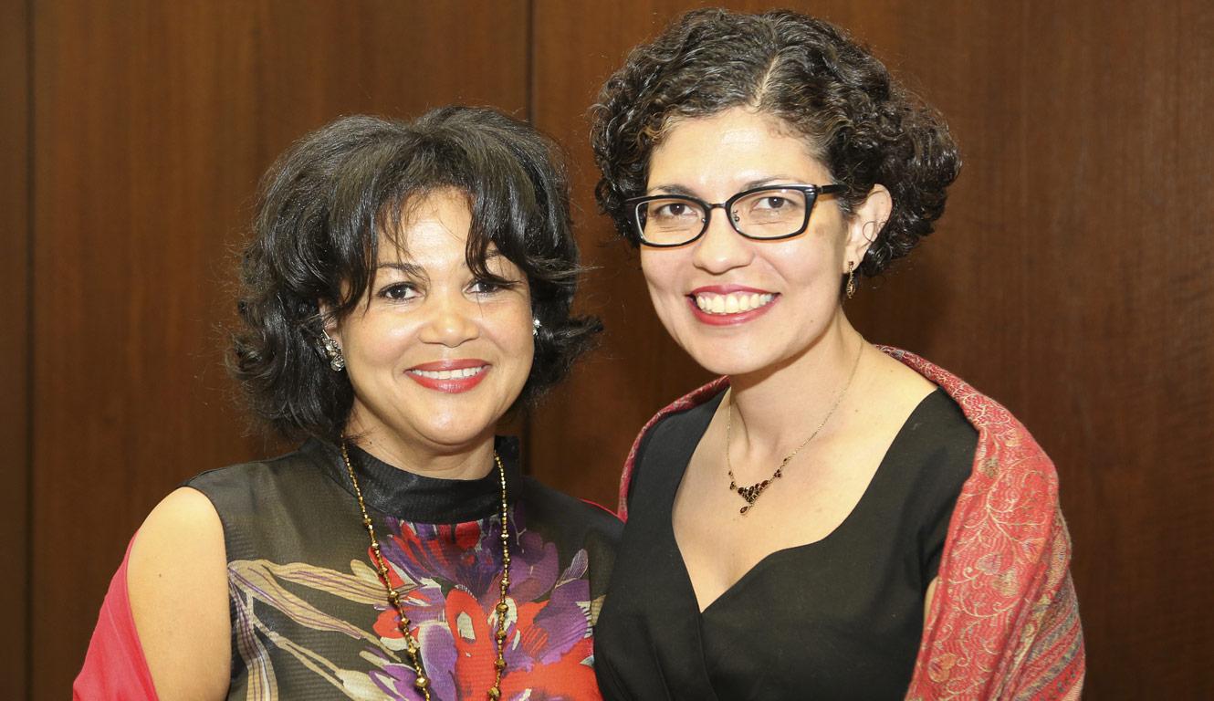 Two fem-presenting people with short, dark hair smile at the camera.