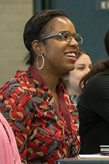 A female-presenting person sits in a classroom and smiles away from the camera.