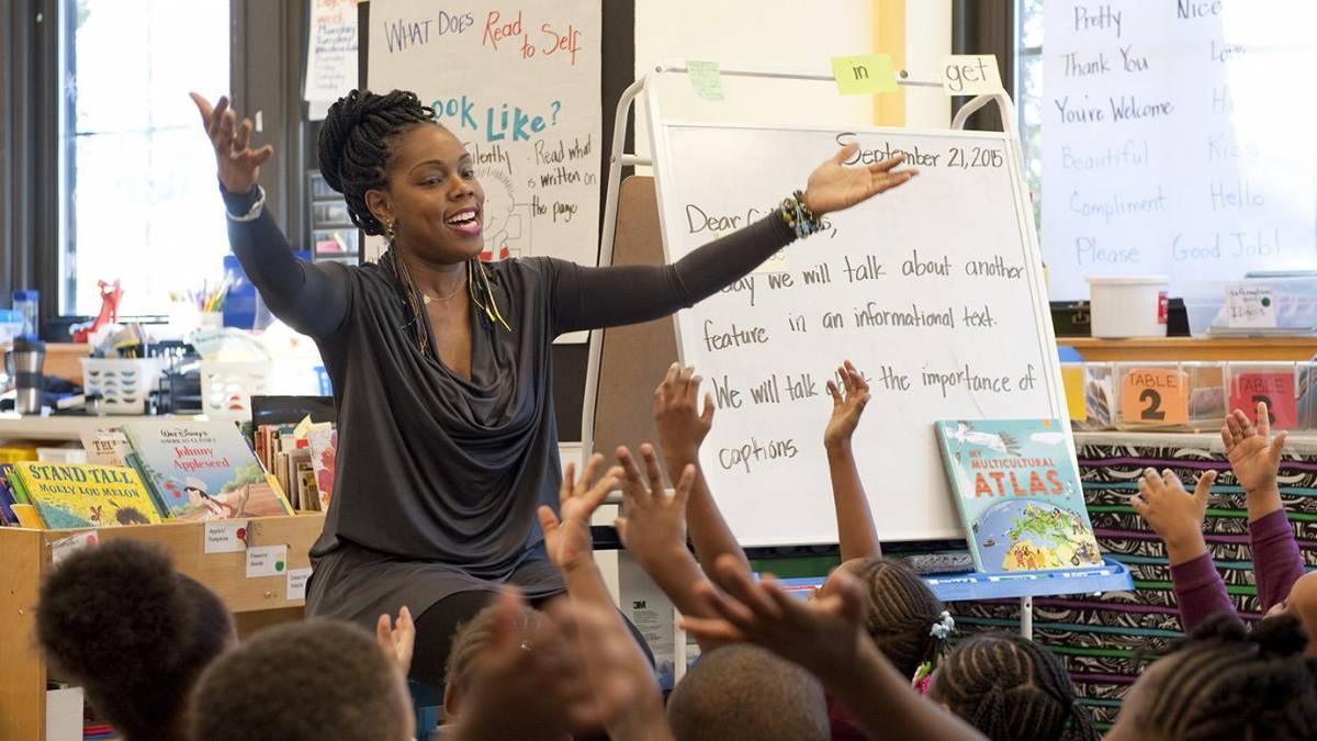 Woman extends her arms towards group of children sitting in a classroom. Photo by Seong-Ah Cho