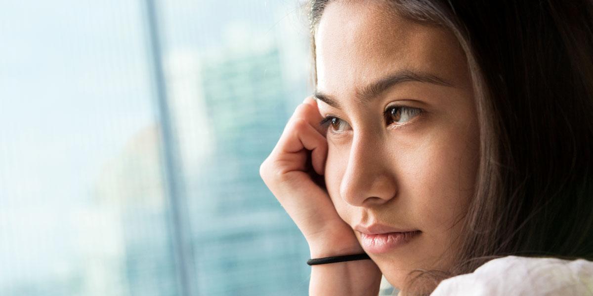 Young woman of asian descent looks out of a window sadly 