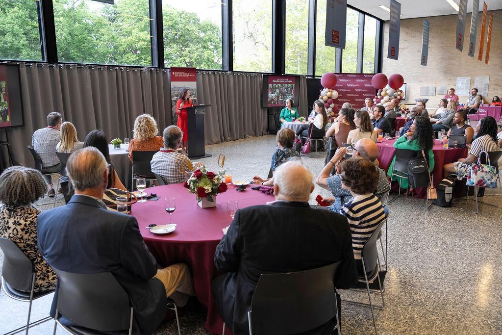 group of people sitting at tables with balloons and woman standing at podium