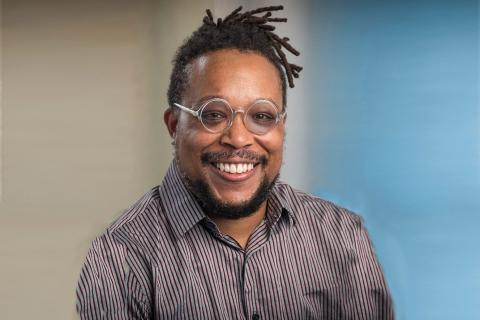 Man in striped brown button up shirt with glasses smiling