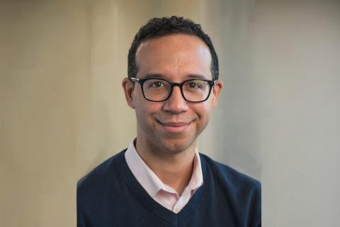 Male in black sweater with pink shirt smiling with glasses