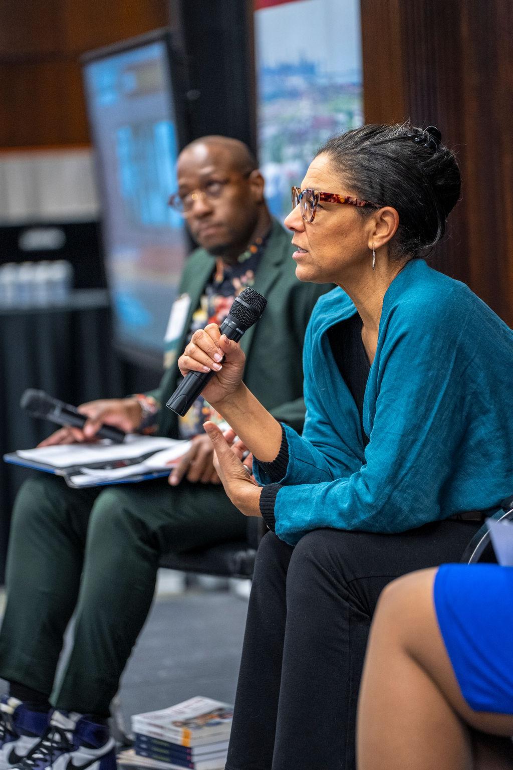 woman holding the microphone in a turquoise blouse with glasses