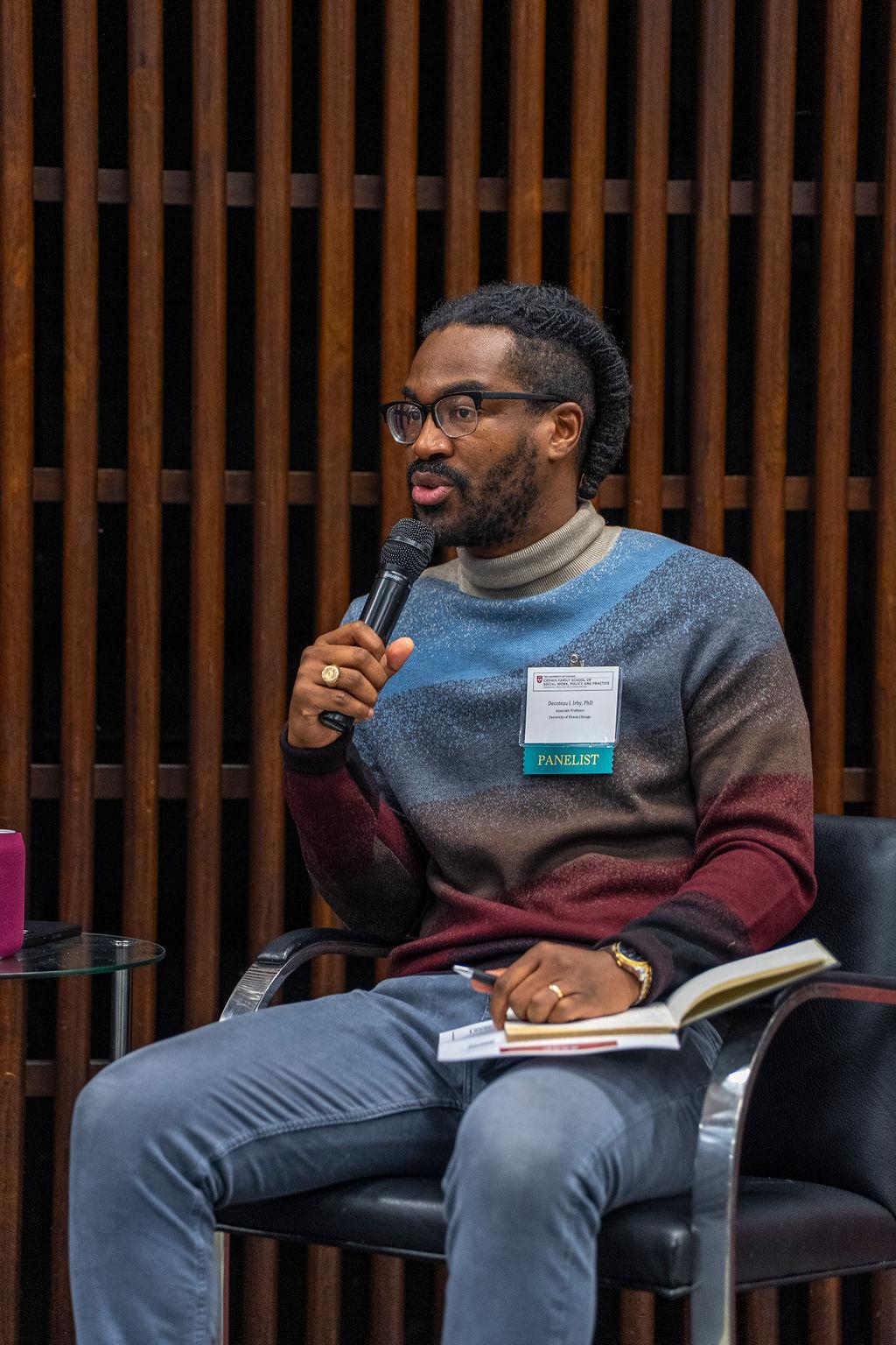 image of man sitting holding a mic speaking with bluejeans and a colorful sweater