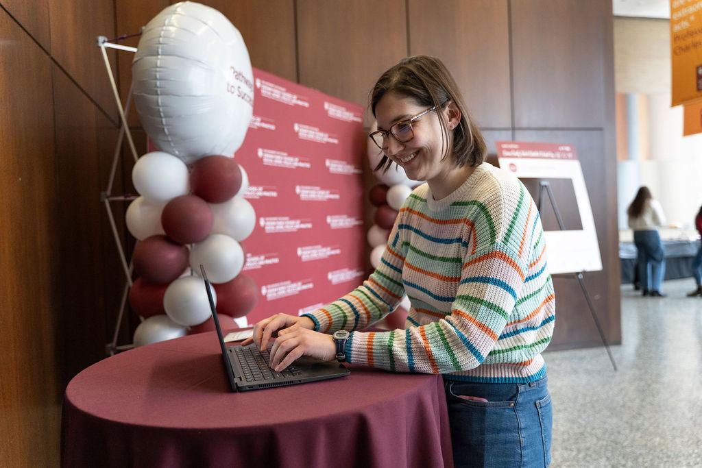 Woman with short light brown hair in stripped sweater typing onto laptop 