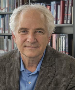 Mark Courtney wearing a blue shirt and suit jacket in front of library shelves