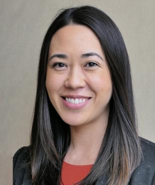 Ashley Brown, a female-presenting person, smiles towards the camera against a light-brown background.