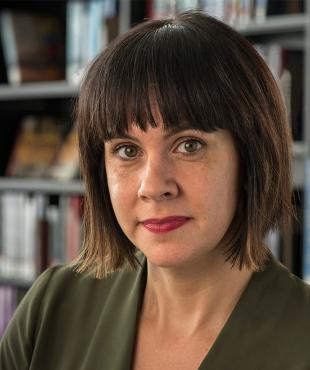 Angela Garcia, a female-presenting person, smiles towards the camera in a library.