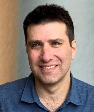 Aaron Gottlieb, a male-presenting person, smiles towards the camera against a grey and orange background.