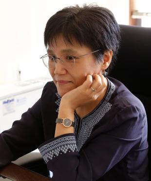 Yoonsun Choi, a female-presenting person, sits in an office and smiles away from the camera.