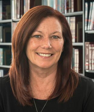 Deborah Gorman-Smith, a female-presenting person, smiles towards the camera in a library.