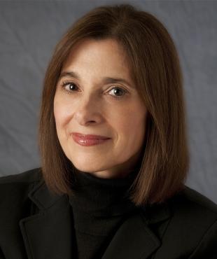 A female-presenting person smiles towards the camera against a dark gray background.