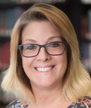 Gidget Ambuehl, a female-presenting person who smiles towards the camera in a library.