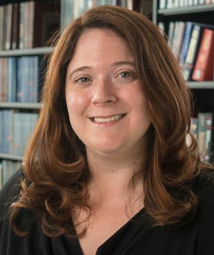 Gina Fedock, a female-presenting person, smiles towards the camera in a library.