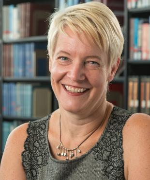 Jessica Darrow, a female-presenting person, smiles towards the camera in a library.