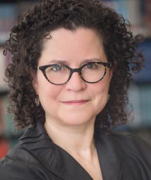 Laura Botwinick, a female-presenting person who smiles towards the camera in a library.