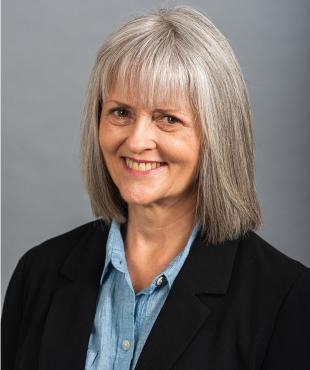 Susan Lambert, a female-presenting person, smiles towards the camera against a light-gray background.
