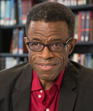 Waldo Johnson, a male-presenting person, smiles towards the camera in a library.