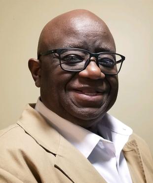 Willie Cobb in white dress shirt, tan suit jacket, and glasses against a tan backdrop