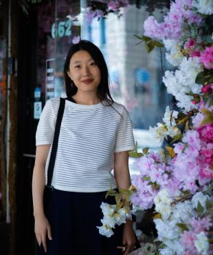 Woman in a white shirt with black skirt smiling in front of flowers