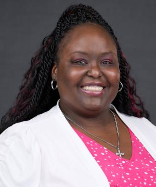 Woman in white shirt with pink and white dots with a ponytail smiling