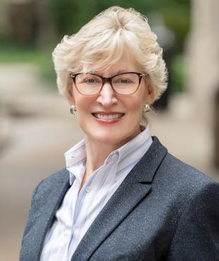 Woman in glasses and short blond cut smiling in a grey blazer with with button up shirt