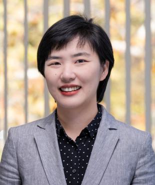 Woman smiling in grey blazer with polk dot shirt in front of a window