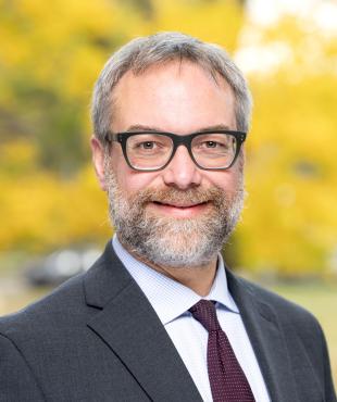 Male in a grey suit with maroon tie with a fall yellow background