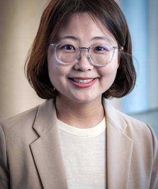 woman in a tan jacket with white shirt smiling with glasses