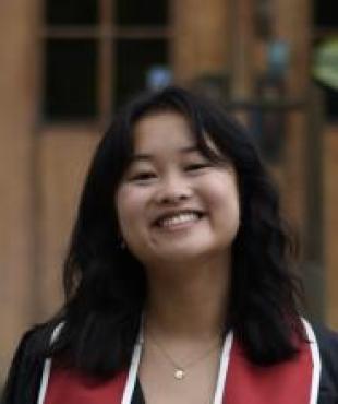 woman smiling in a graduation robe with red and white stole