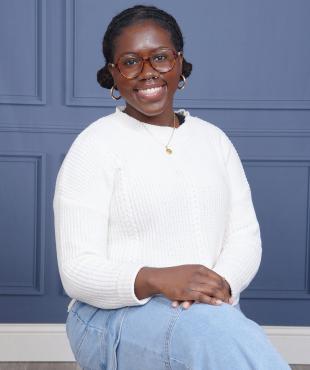 Woman, sitting, white blouse, jeans, with glasses, smiling,  blue backdrop