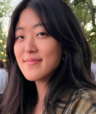 Woman, standing, brown and grey top, smiling , black hair, outdoors